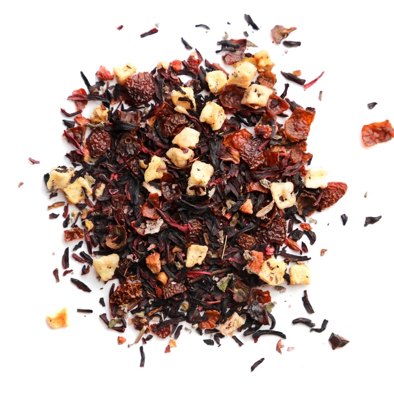 May include: A close-up of a blend of dried fruit and herbs for tea. The mix includes dried apple pieces, hibiscus flowers, and other red berries.