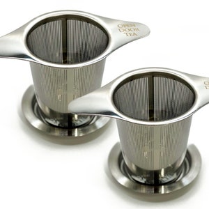 May include: Two stainless steel tea infusers with handles and a base. The infusers have a fine mesh and the handles are engraved with the words "Open Door Tea".