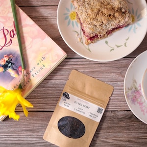 May include: A brown paper pouch of loose leaf Pu-Erh Berry tea with a clear window showing the dark tea leaves. The pouch has text that reads "Open Doorlia Pu-Erh Berry Boiling Water Steep 3-5 Minutes 1 Teaspoon Per Cup".