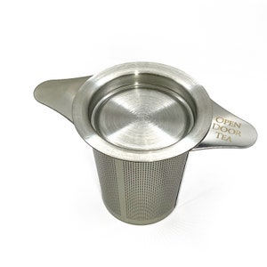 May include: Stainless steel tea infuser with a lid and two handles. The infuser has a fine mesh and the text "OPEN DOOR TEA" is engraved on one of the handles.