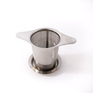 May include: A stainless steel tea infuser with a handle and a mesh filter. The infuser has a base that sits on the bottom of a cup or teapot. The infuser has the words "Open Door Tea" printed on the handle.