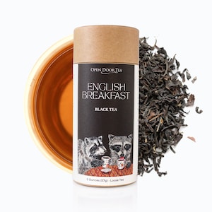 May include: A brown cardboard tube with a black and white label that says "OPEN DOOR TEA ENGLISH BREAKFAST BLACK TEA". The label also features a cartoon illustration of two raccoons drinking tea. The tube contains 2 ounces (57g) of loose leaf tea.