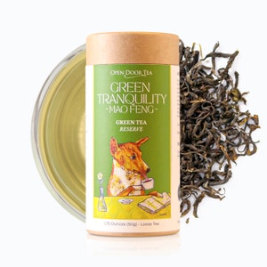 May include: A cylindrical container of "Green Tranquility - Mao Feng - Green Tea Reserve" loose tea, with a cartoon dog illustration. The container is next to a pile of loose tea leaves and a cup of tea. The container holds 1.75 ounces (50g) of tea.