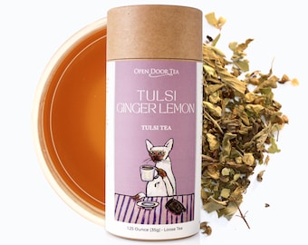 May include: A brown cardboard tube with a pink and white label. The label features a cartoon cat drinking tea and the text "Tulsi Ginger Lemon Tulsi Tea 1.25 Ounce (35g) - Loose Tea".