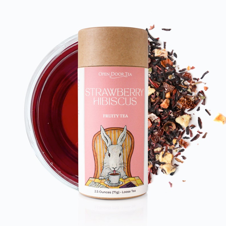 May include: A brown tube with a pink label that says "OPEN DOOR TEA STRAWBERRY HIBISCUS FRUITY TEA". The label also features a cartoon rabbit sitting in a chair with a cup of tea. The tube contains 2.5 ounces (71g) of loose leaf tea.
