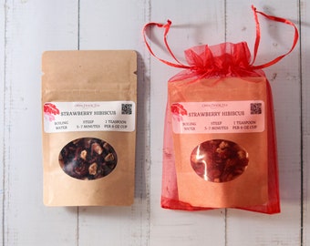 May include: Two packages of loose leaf tea, one in a brown paper pouch and the other in a red mesh bag. Both packages contain dried strawberry hibiscus tea and have a label that reads "OPEN DOOR TEA STRAWBERRY HIBISCUS BOILING WATER STEEP 5-7 MINUTES 1 TEASPOON PER 6 OZ CUP".