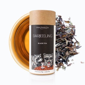 May include: A brown cardboard tube with a black label that says "Open Door Tea" and "Darjeeling Black Tea". The label also features an illustration of two raccoons drinking tea. The tube contains 2 ounces (57g) of loose leaf tea.