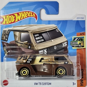 May include: A brown and gold custom Volkswagen T3 van toy car with the text "VW T3 CUSTOM" and "793" on the side. The car is on a blue and white background with the Hot Wheels logo.