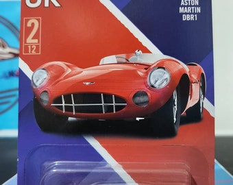 May include: A red 1956 Aston Martin DBR1 toy car in a Matchbox UK 2/12 packaging. The car has a black interior and black wheels. The packaging has a Union Jack design.