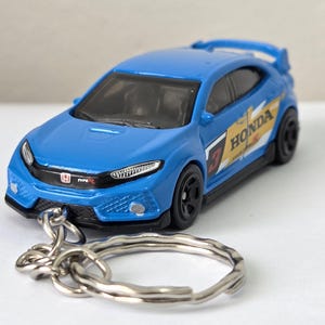 May include: A blue Honda Civic Type R model car keyring. The miniature car has black wheels, a rear spoiler, and the Honda logo. The side of the car features the word "HONDA" and the number "3" in a yellow and white design.