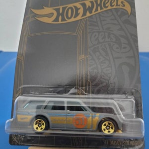 May include: A gray 1971 Datsun 510 Wagon Hot Wheels car in a black and gold packaging with the Hot Wheels logo. The car has a gold 51 on the side.