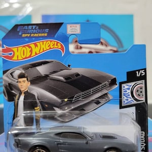 May include: A gray Hot Wheels die-cast toy car with black racing stripes. The car is part of the Fast & Furious Spy Racers collection and is labeled "Rod Squad".
