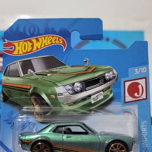 May include: Green die-cast toy car model of a Toyota Celica with gold wheels and orange and black racing stripes. The car is in a plastic blister pack with the Hot Wheels logo and the words "JDM Imports" on the side. The car is number 3/10 in the series.