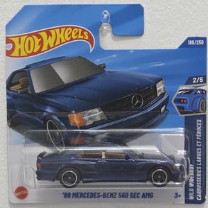 May include: A blue Hot Wheels die-cast toy car of a '89 Mercedes-Benz 560 SEC AMG. The car is displayed in a clear plastic package with the Hot Wheels logo and the text "WILD WIDEBODY". The package also includes the numbers 186/250 and 2/5.