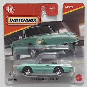 May include: A Matchbox toy car of a '67 Alfa Romeo Duetto in a light teal color. The toy car is on a red and yellow cardboard backing with the Matchbox logo and the text "Designed for a Lifetime". The packaging also includes the text "04/125".
