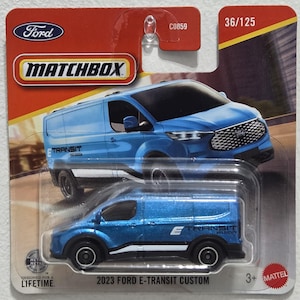 May include: A Matchbox die-cast model of a 2023 Ford E-Transit Custom van. The van is a vibrant blue with black wheels and white accents. The packaging includes the Ford and Matchbox logos, along with the text "2023 Ford E-Transit Custom".