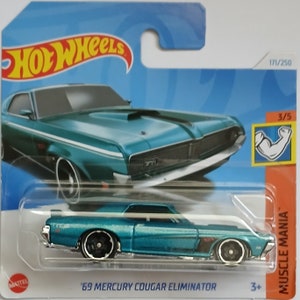 Puede incluir: Un coche de fundición a presión Hot Wheels de color azul verdoso, un Mercury Cougar Eliminator de 1969. El coche tiene una parrilla negra y ruedas negras. El coche está en una tarjeta azul y naranja con las palabras "Hot Wheels" y "Muscle Mania".