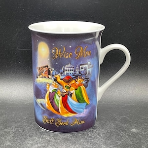 May include: A white ceramic mug with a blue and gold design featuring the Wise Men following a star. The text "Wise Men Still Seek Him" is printed on the mug.