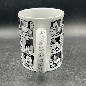 Pu&ograve; includere: Tazza in ceramica bianca con un design in bianco e nero di Topolino che spunta da quadrati. Il manico della tazza ha un design ripetuto della mano di Topolino.