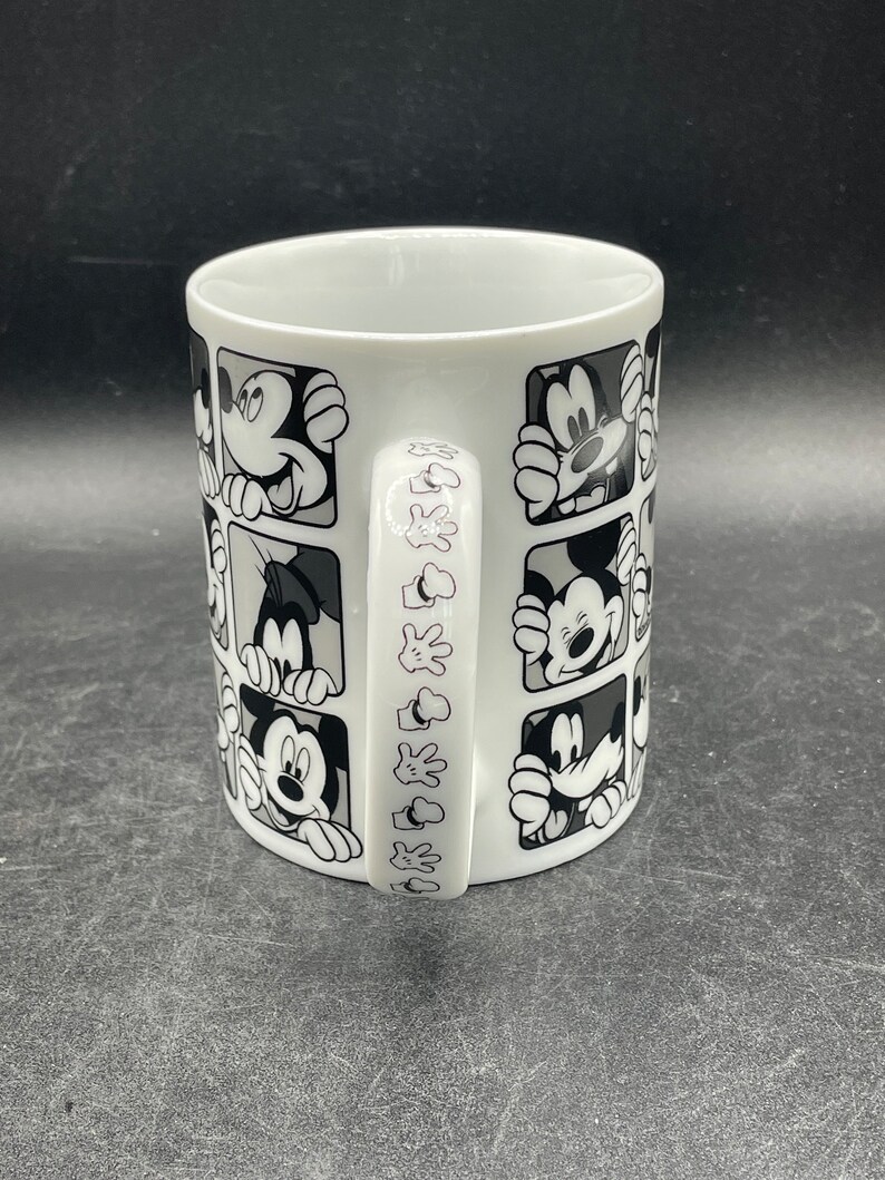 Pu&ograve; includere: Tazza in ceramica bianca con un design in bianco e nero di Topolino che spunta da quadrati. Il manico della tazza ha un design ripetuto della mano di Topolino.
