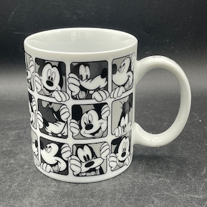 Pu&ograve; includere: Tazza in ceramica bianca con un design in bianco e nero di volti di Topolino in diverse pose. La tazza ha un manico sul lato destro.