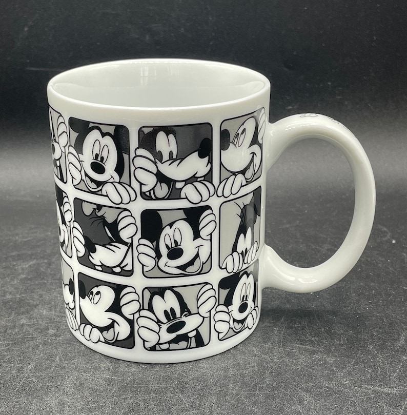 Pu&ograve; includere: Tazza in ceramica bianca con un design in bianco e nero di volti di Topolino in diverse pose. La tazza ha un manico sul lato destro.