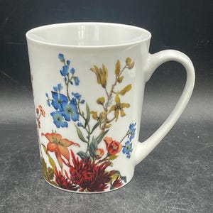 May include: White ceramic mug with a floral design featuring blue, red, orange, and yellow flowers.