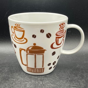 May include: White ceramic coffee mug with a brown and orange design featuring coffee cups, coffee beans, and a french press.