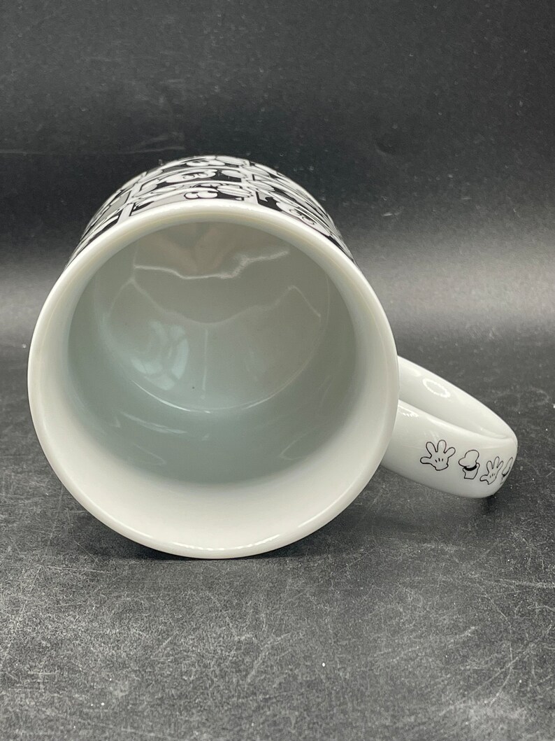 Pu&ograve; includere: Tazza in ceramica bianca con un design bianco e nero di mani di Topolino sul manico e un design bianco e nero di teste di Topolino sul lato della tazza.