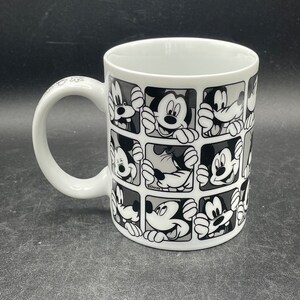 Pu&ograve; includere: Tazza in ceramica bianca con un design bianco e nero di Topolino che spunta da quadrati. La tazza ha un manico nero.