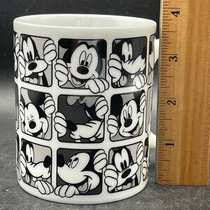 Pu&ograve; includere: Tazza in ceramica bianca con un design bianco e nero di volti di Topolino in quadrati.
