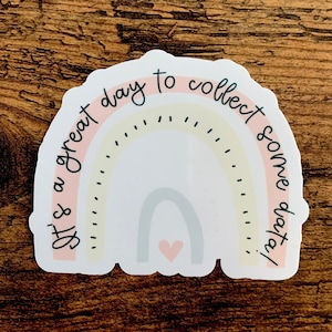 Könnte beinhalten: Ein Regenbogen-Aufkleber mit dem Text "It's a great day to collect some days". Der Regenbogen ist in den Farben Rosa, Gelb und Blau mit einem kleinen Herzen in der Mitte.
