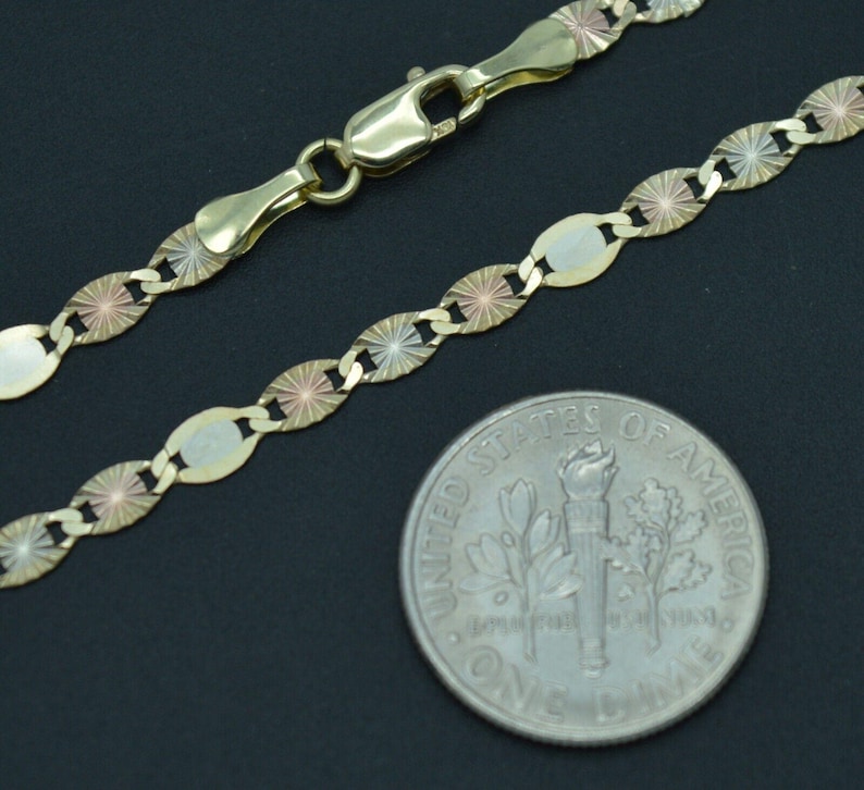 May include: A gold chain necklace with a tri-colour design. The chain is made of oval links with a starburst pattern. The chain is shown next to a US dime for size comparison.