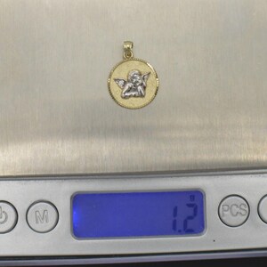 May include: A gold pendant with a white angel design. The pendant is on a digital scale that reads 1.2 grams.