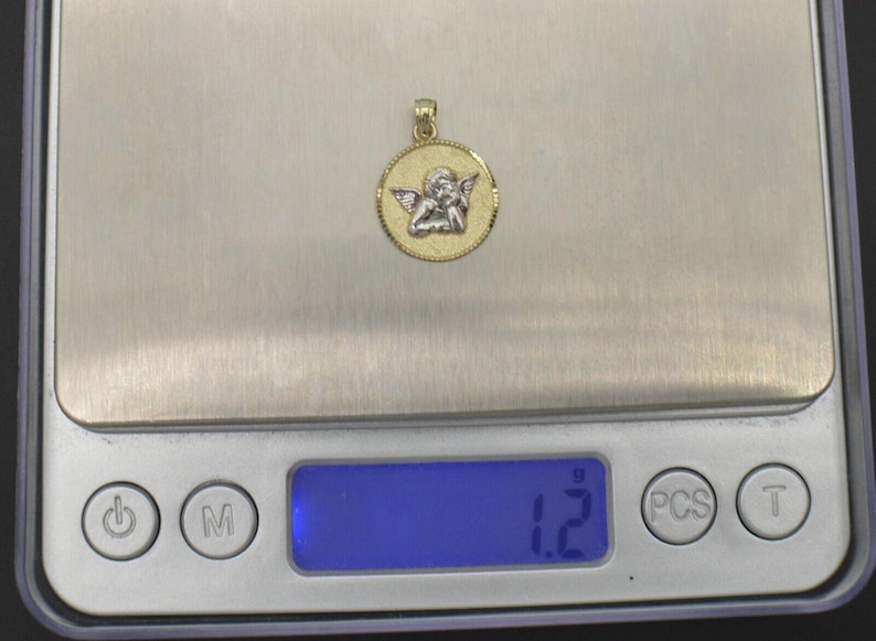 May include: A gold pendant with a white angel design. The pendant is on a digital scale that reads 1.2 grams.