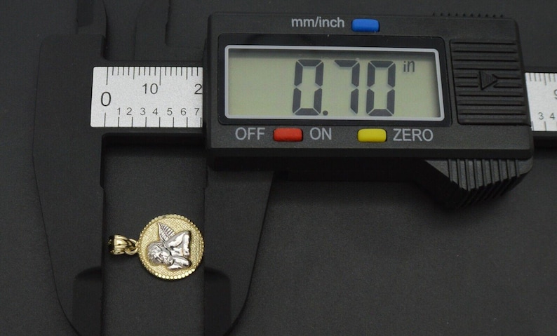 May include: A gold and white angel pendant charm, measuring 0.70 inches in diameter, is shown next to a digital caliper.