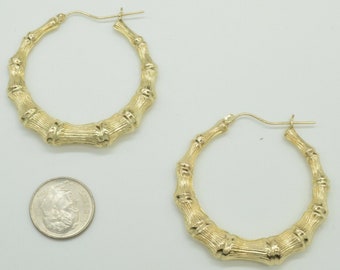 May include: A pair of gold bamboo hoop earrings. The earrings are large and have a textured surface. The earrings are shown next to a US dime for size comparison.