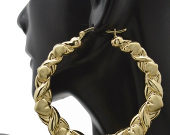 May include: Gold hoop earrings with a heart-shaped design. The earrings are thick and have a twisted rope-like texture.