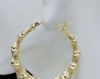 May include: Gold bamboo hoop earrings. The earrings are made of a thick, textured gold metal and are shaped like bamboo stalks. The earrings are large and have a diameter of about 2 inches.