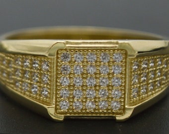 May include: A gold ring with a square-shaped center set with small, clear stones. The band of the ring is also set with small, clear stones.