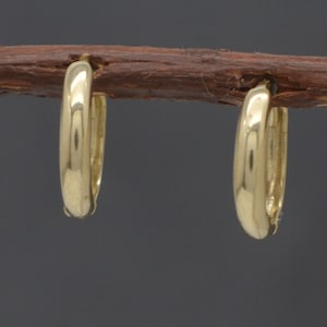 May include: A pair of polished gold hoop earrings with a smooth, rounded surface. The earrings are circular in shape and feature a reflective, metallic finish. Each hoop is designed with a simple, continuous band that creates a clean, classic look.