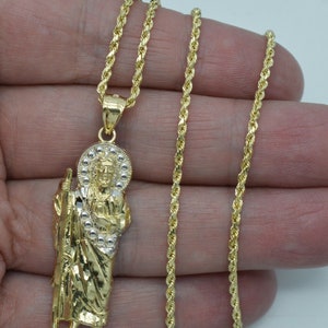 May include: A gold rope chain necklace with a pendant featuring a detailed depiction of a religious figure. The pendant is two-toned, with a gold and silver finish.