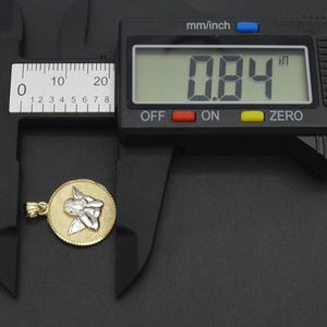 May include: A gold pendant with a silver angel design, measured at 0.84 inches with a digital caliper.