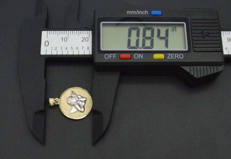 May include: A gold pendant with a silver angel design, measured at 0.84 inches with a digital caliper.