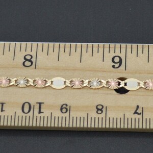 May include: A gold chain necklace with a three-tone design, featuring yellow, rose, and white gold. The chain is measured against a ruler, showing it is approximately 8 inches (20 cm) long.