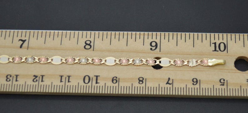 May include: A gold chain necklace with a three-tone design, featuring yellow, rose, and white gold. The chain is measured against a ruler, showing it is approximately 8 inches (20 cm) long.