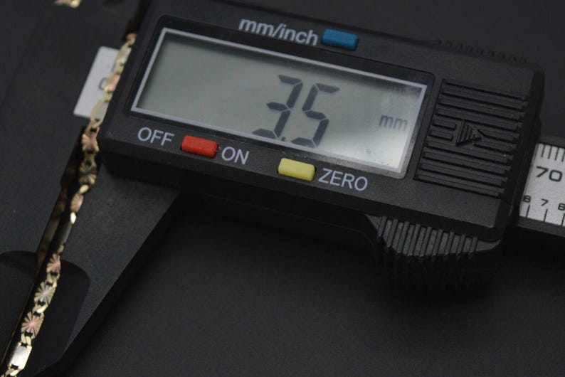 May include: A black digital caliper measuring 3.5 mm. The caliper has a black display with white numbers, red and yellow buttons, and a black and silver handle.