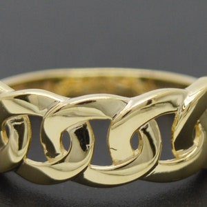 May include: A gold-coloured ring featuring a chain link design. The ring is made of a shiny, reflective metal with a smooth surface. The chain links are interlocked, forming a continuous band.