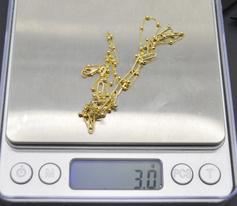 May include: A gold-toned chain necklace featuring a combination of elongated oval links and small spherical beads. The necklace is resting on a digital scale that displays a weight of 3.0 grams, providing a clear measurement of the jewellery piece.