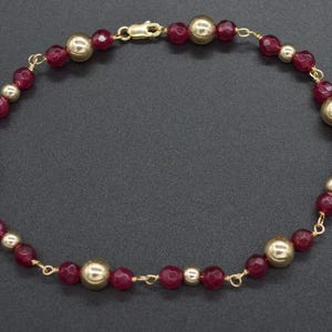 May include: A gold and burgundy beaded bracelet with a delicate chain. The bracelet features alternating round gold and faceted burgundy beads.